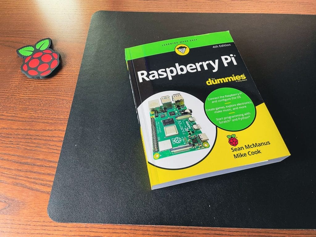 A book called "Raspberry Pi for Dummies (4th Edition)" sits on a desk next to a Raspberry Pi drinks coaster